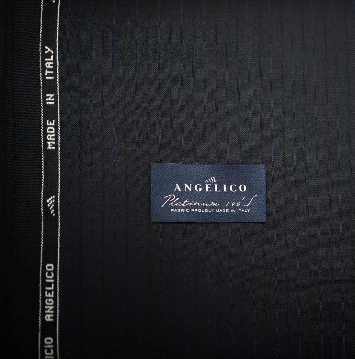 Charcoal Angelico pinstripe suiting rolled beside its Platinum selvedge label and Made in Italy edge