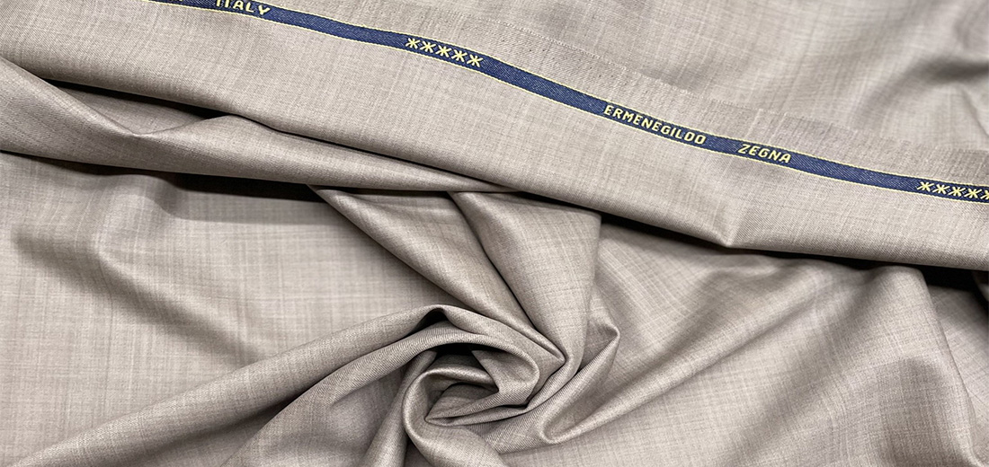 Fawn Ermenegildo Zegna cloth draped in soft folds beside its woven selvedge